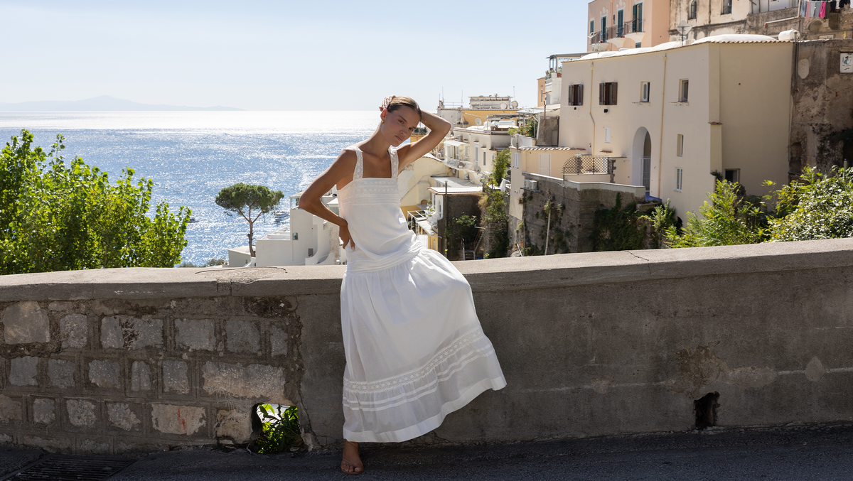Model in the Aurora white maxi dress sitting on a wall above the sea in Positano