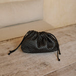 Black woven leather Naomi Clutch on a wooden bench on the Nusa islands